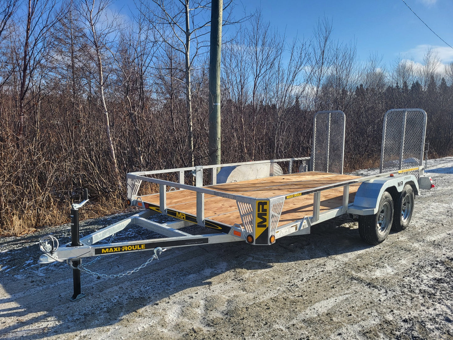 Maxi-Roule galvanized double axle trailer showing sturdy frame, mesh ramps, and wood deck for heavy-duty hauling.