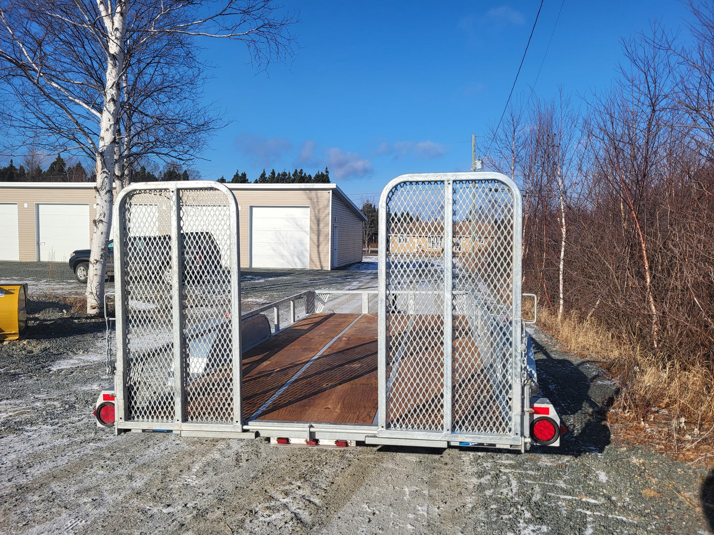 Maxi-Roule galvanized double axle trailer rear view with dual fold-down mesh ramps and reflective safety lighting.