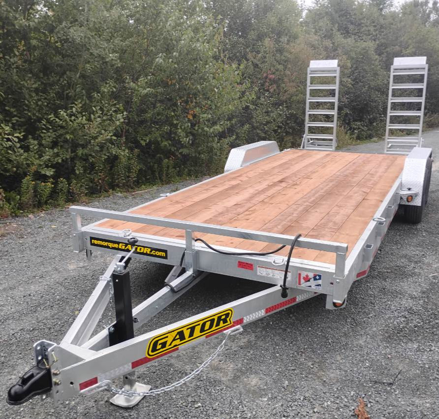 Aluminum trailer with a wooden platform on a gravel road with trees in the background