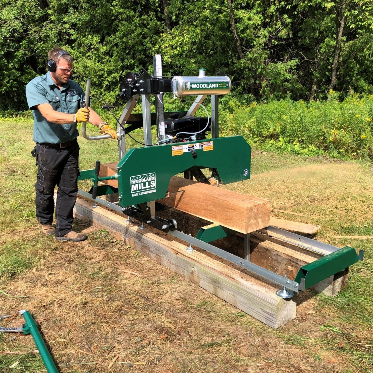 Man operating Woodland HM122 Portable Sawmill in an outdoor setting with trees in the background